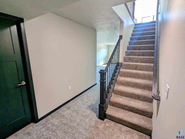 stairway featuring light carpet and a textured ceiling