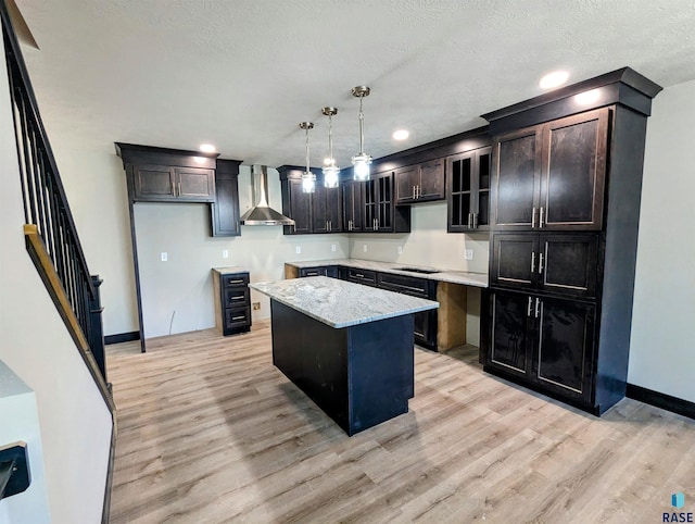 kitchen featuring hanging light fixtures, light hardwood / wood-style floors, a kitchen island, and wall chimney range hood