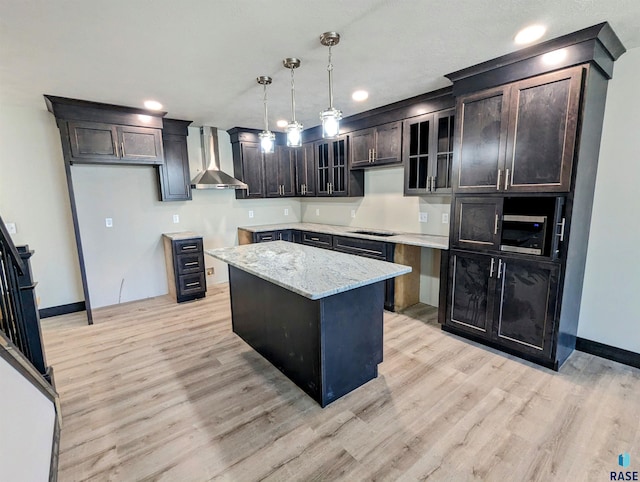 kitchen with light hardwood / wood-style flooring, hanging light fixtures, light stone counters, and wall chimney exhaust hood