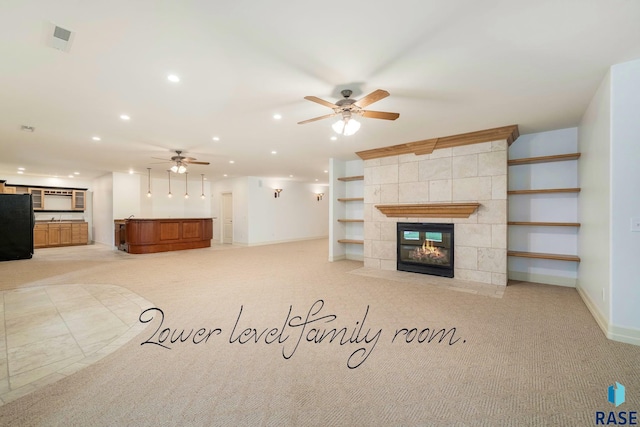 unfurnished living room with ceiling fan, light colored carpet, built in shelves, and a tiled fireplace