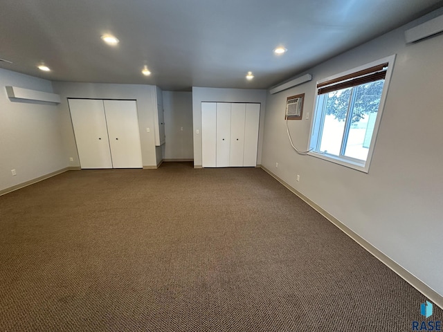 unfurnished bedroom with carpet floors, a wall mounted AC, and two closets