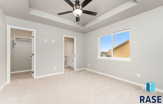 unfurnished bedroom featuring a tray ceiling, a walk in closet, ceiling fan, and ensuite bath