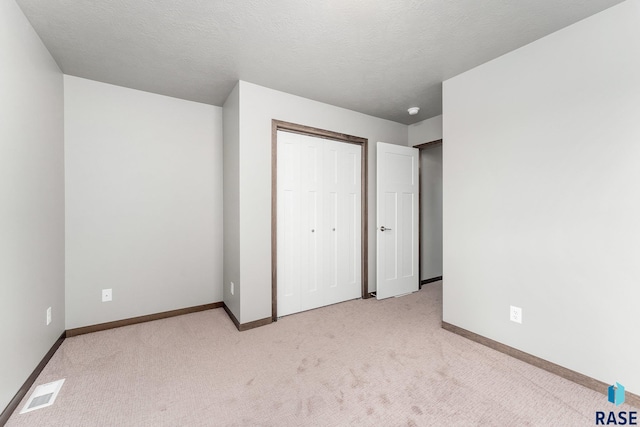 unfurnished bedroom featuring light carpet, a closet, and a textured ceiling