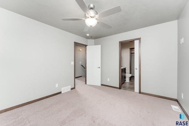 unfurnished bedroom featuring light colored carpet, a spacious closet, ceiling fan, and ensuite bathroom