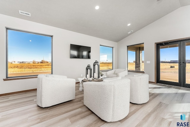 living room with french doors, a healthy amount of sunlight, vaulted ceiling, and light hardwood / wood-style flooring