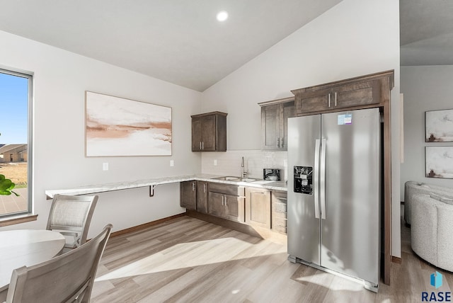 kitchen with vaulted ceiling, sink, stainless steel fridge, decorative backsplash, and dark brown cabinets