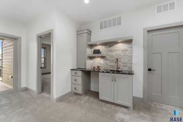 kitchen with dark stone counters, sink, light carpet, and tasteful backsplash