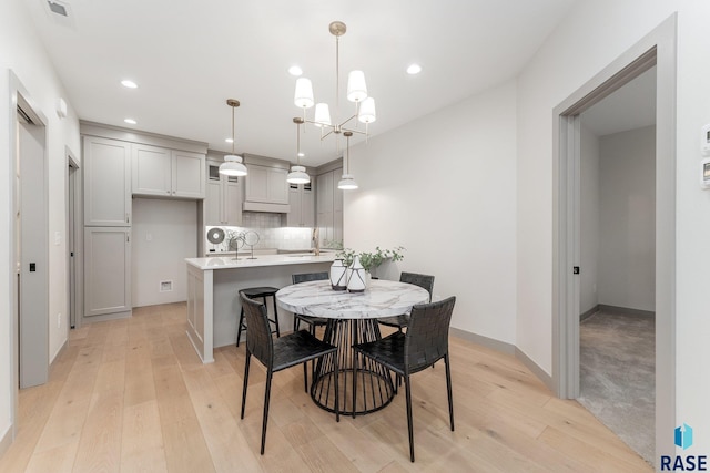 dining area featuring an inviting chandelier, sink, and light wood-type flooring