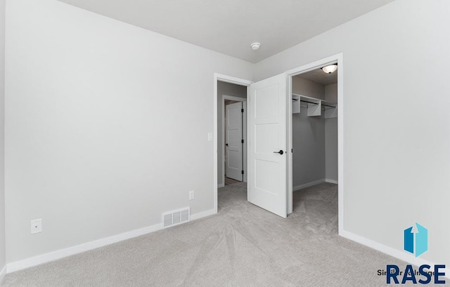 unfurnished bedroom with light colored carpet, a spacious closet, and a closet