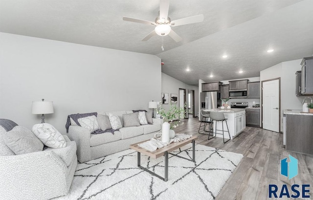 living room with ceiling fan, light wood-type flooring, and vaulted ceiling