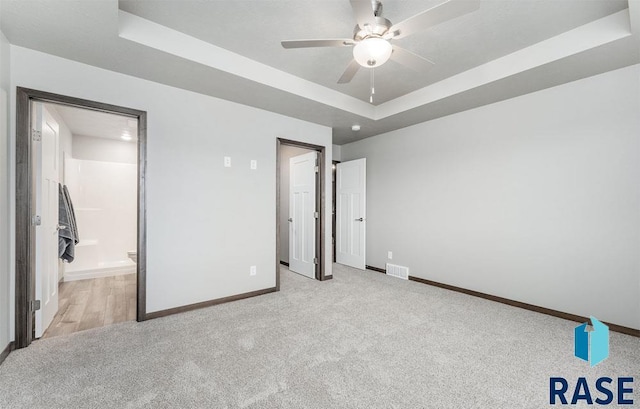 unfurnished bedroom with a tray ceiling, connected bathroom, ceiling fan, and light carpet