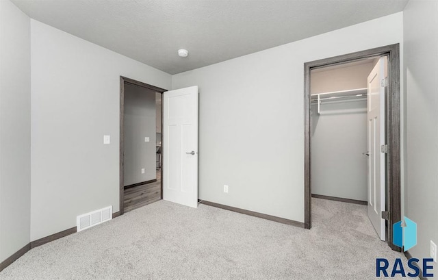 unfurnished bedroom with a walk in closet, a closet, and light colored carpet