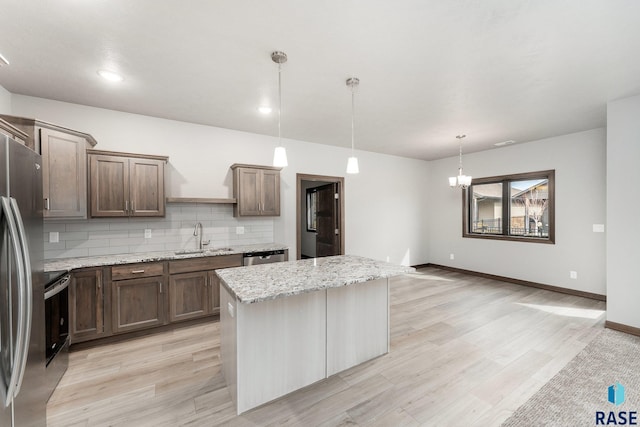 kitchen with appliances with stainless steel finishes, decorative light fixtures, light stone counters, a center island, and decorative backsplash