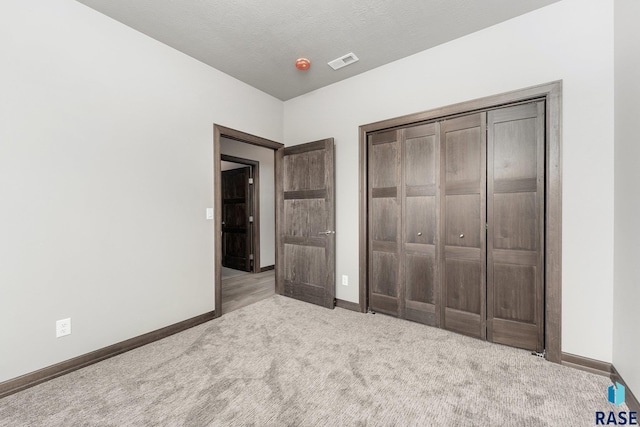 unfurnished bedroom with light carpet, a textured ceiling, and a closet