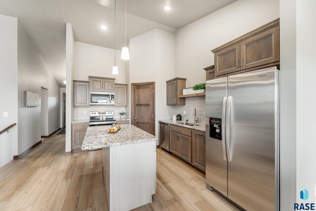 kitchen featuring appliances with stainless steel finishes, tasteful backsplash, a towering ceiling, and light wood-type flooring