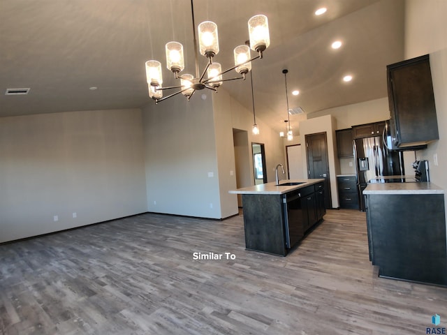 kitchen with lofted ceiling, pendant lighting, sink, a kitchen island with sink, and light wood-type flooring