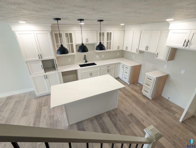 kitchen featuring decorative light fixtures, white cabinets, light wood-type flooring, sink, and a textured ceiling