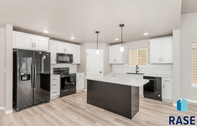 kitchen featuring decorative light fixtures, white cabinetry, a center island, black appliances, and light hardwood / wood-style flooring