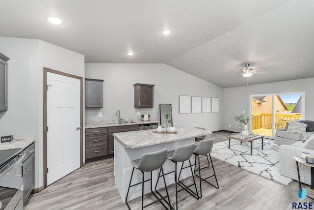 kitchen with light wood-type flooring, ceiling fan, sink, a center island, and a breakfast bar area