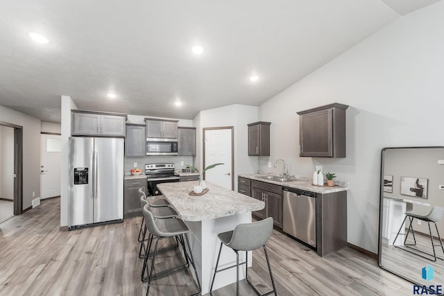 kitchen featuring sink, light hardwood / wood-style floors, a kitchen bar, a kitchen island, and appliances with stainless steel finishes