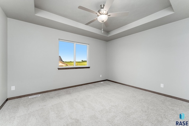 carpeted spare room with a raised ceiling and ceiling fan