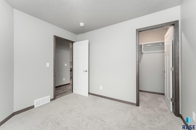 unfurnished bedroom with a walk in closet, light carpet, and a closet