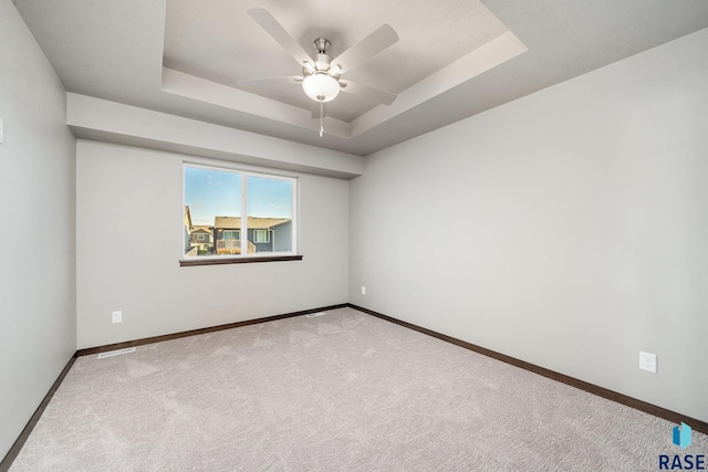 unfurnished room featuring ceiling fan, light colored carpet, and a tray ceiling