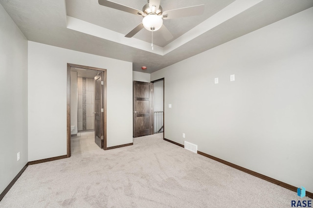 unfurnished bedroom with light colored carpet, a raised ceiling, ceiling fan, and ensuite bathroom