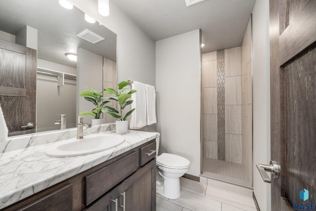 bathroom with tiled shower, vanity, toilet, and tile patterned floors