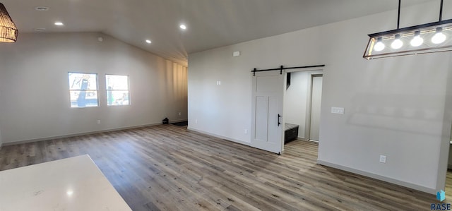 unfurnished room featuring hardwood / wood-style floors, vaulted ceiling, and a barn door