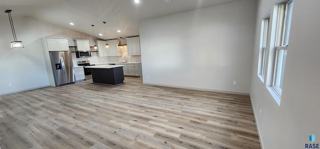 kitchen with appliances with stainless steel finishes, a kitchen island, sink, light wood-type flooring, and hanging light fixtures