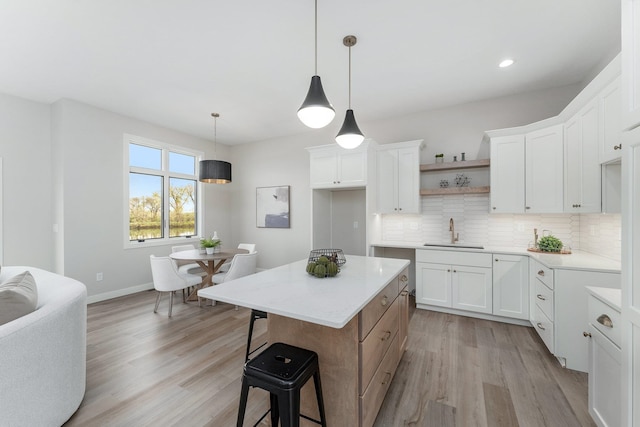 kitchen with hanging light fixtures, light hardwood / wood-style floors, white cabinets, a kitchen island, and sink