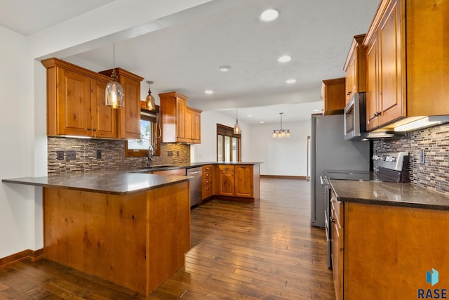 kitchen with kitchen peninsula, stainless steel appliances, pendant lighting, dark wood-type flooring, and backsplash