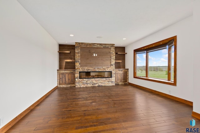 unfurnished living room featuring a stone fireplace, dark wood-type flooring, and wooden walls