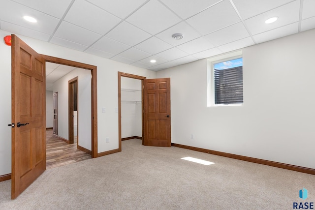 unfurnished bedroom with a walk in closet, a closet, hardwood / wood-style flooring, and a paneled ceiling