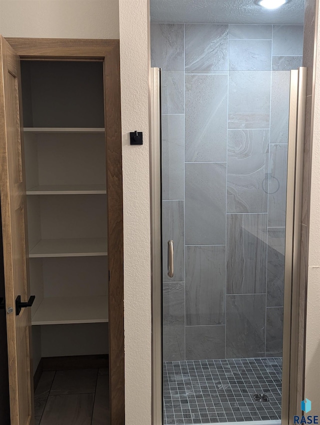 full bathroom featuring a shower stall, a spacious closet, and a textured wall