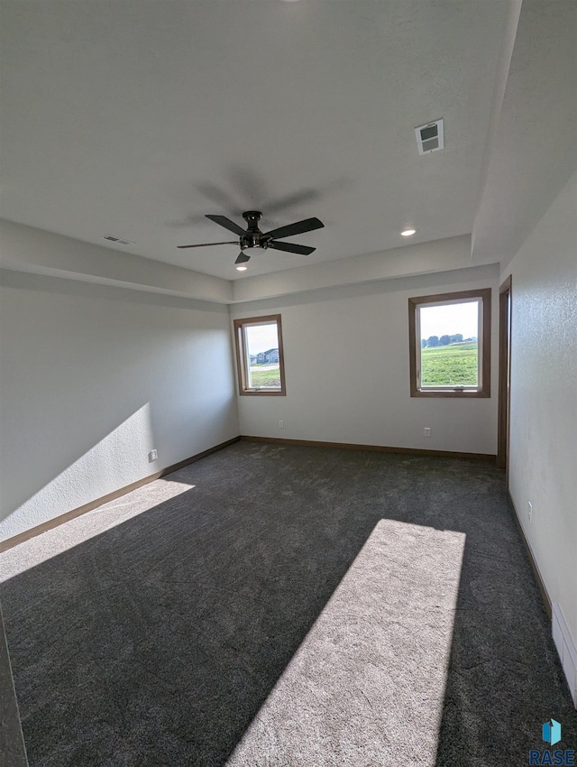 empty room featuring ceiling fan, baseboards, visible vents, and dark carpet