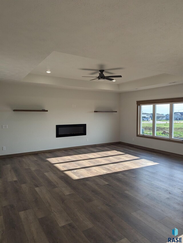 unfurnished living room with ceiling fan, a tray ceiling, and wood-type flooring