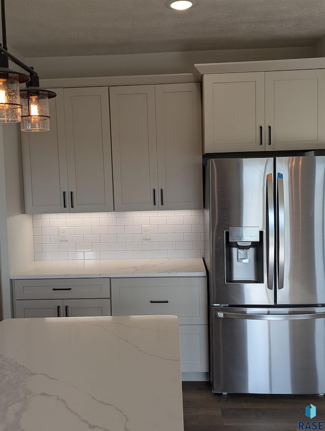 kitchen with dark wood finished floors, light stone counters, stainless steel refrigerator with ice dispenser, and backsplash