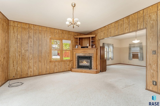 unfurnished living room featuring light colored carpet, wooden walls, and a chandelier