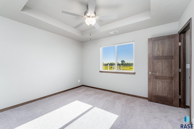 carpeted spare room with ceiling fan and a raised ceiling