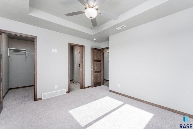 bedroom featuring ceiling fan, a closet, light carpet, and a tray ceiling