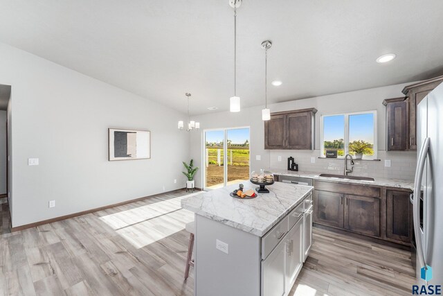 kitchen with a center island, sink, light stone counters, backsplash, and pendant lighting