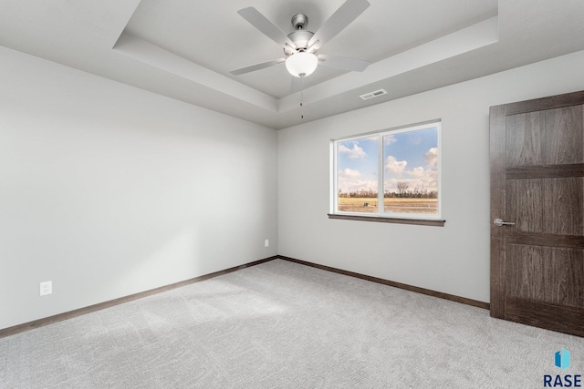 empty room featuring light colored carpet, a raised ceiling, and ceiling fan