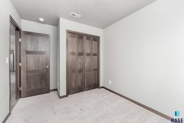 unfurnished bedroom with light colored carpet and a closet