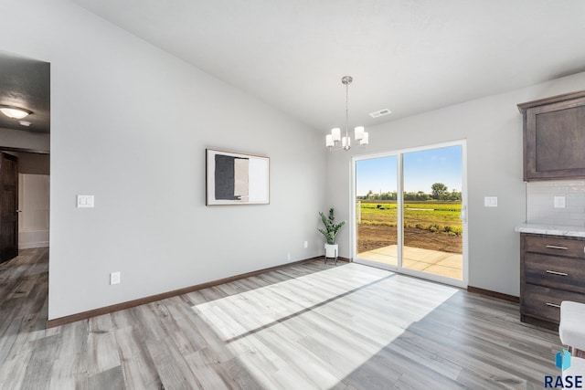 unfurnished dining area with a chandelier, light wood-type flooring, and vaulted ceiling