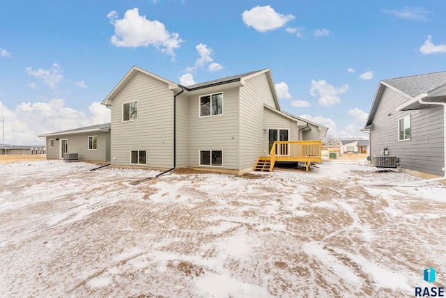 snow covered rear of property with central AC unit and a deck