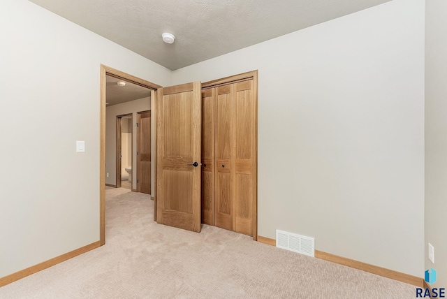 unfurnished bedroom featuring a closet, light colored carpet, and a textured ceiling