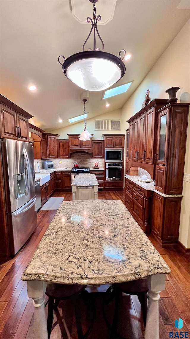 kitchen with dark hardwood / wood-style floors, vaulted ceiling with skylight, a kitchen island, hanging light fixtures, and appliances with stainless steel finishes