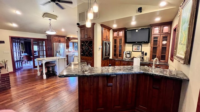 kitchen with a kitchen breakfast bar, dark stone countertops, dark hardwood / wood-style floors, stainless steel refrigerator with ice dispenser, and pendant lighting